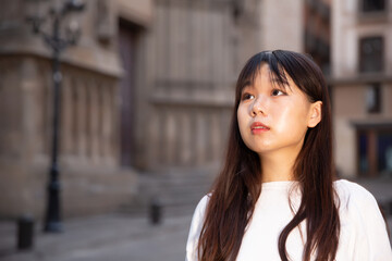 Obraz premium Portrait of cheerful young chinese longhaired woman standing on a city street. High quality photo
