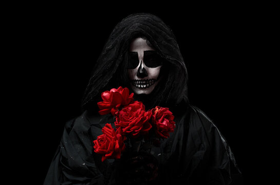 woman in a black hood with a skeleton make-up holds a bouquet of red roses