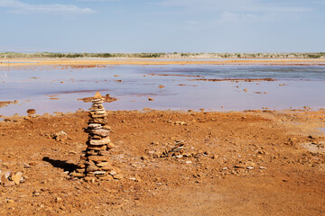 Muddy ground with spring water, with stacks of stones on one side.