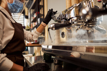 Woman waiter cleaning coffee machine in the cafe bar