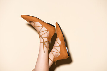 cropped view of female legs in brown suede flat shoes on beige background