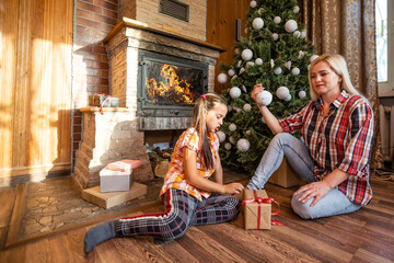 Mom and daughter playing with balls near the Christmas tree. gifts, lights, balls in the background.
