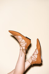 cropped view of female legs in brown suede flat shoes on beige background