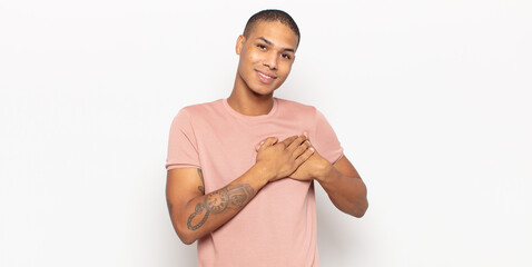 young black man feeling romantic, happy and in love, smiling cheerfully and holding hands close to...