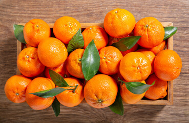 Fresh mandarin oranges fruit or tangerines with leaves in a wooden box