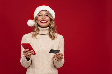 Excited girl in Santa Claus hat showing cellphone and credit card