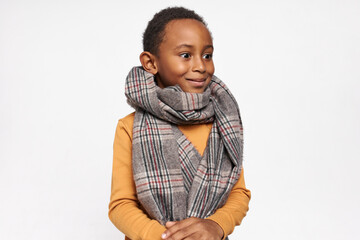 Childhood concept. Isolated image of emotional surprised cute black boy wearing warm scarf smiling and popping out his eyes as if seeing something interesting, expressing excitement or astonishment