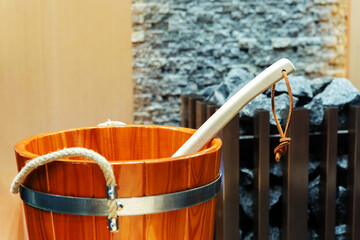 A fragment of a wooden bucket in the bath. Equipment for a sauna on a background of a fireplace with stones