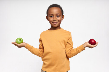 Portrait of confident black boy with cheerful smile posing isolated with green and red apples in...