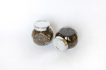 Black peppercorns in jar on white table, flat lay
