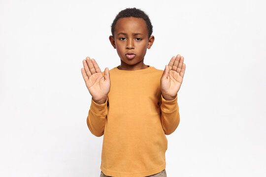 Studio image of serious confident African American schoolboy in sweatshirt reaching out his hands with palms open making stop gesture, saying No, Enough, expressing disagreement. Signs and symbols