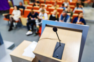 Microphone on the background of people sitting in the conference room. Preparation before the speaker. Blurred background. Unrecognizable people