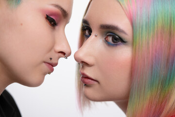 Young lesbian woman couple with vivd colored short hair and jackets posing on white background. Piercing on the face, tunnels in the ears.