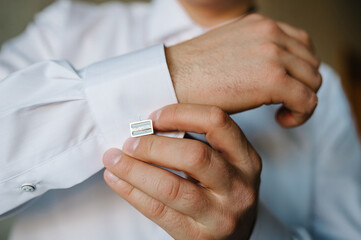 Obraz na płótnie Canvas Hand's groom wears a metallic silver cufflinks stud. Wedding morning.