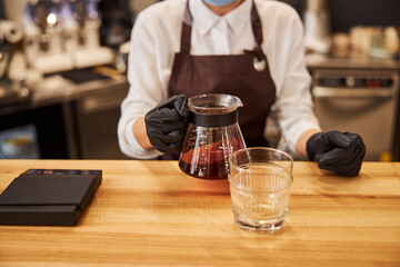 Woman holding kettle with coffee or tea near the glass