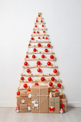Modern creative Christmas eco tree made of wooden branches hanging on white wall with festive lights and gift boxes on the floor. Simple, minimal conscientious interior design. Vertical orientation