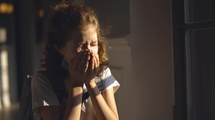 Sick schoolgirl putting removing facial mask and sneezing standing in corridor