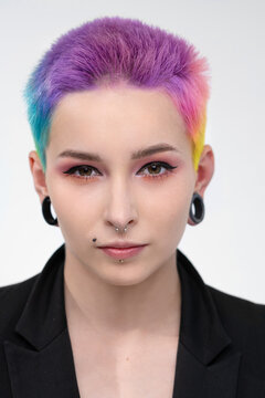 A young beautiful girl with short colored hair. Spread bright coloring and creative make-up. Piercing on the face. A black jacket.