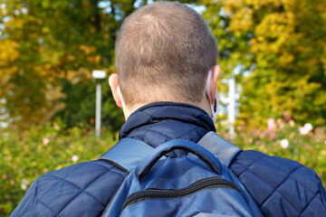 a man in a blue jacket and a blue backpack stands with his back against the background of trees with yellow and green leaves on an autumn day