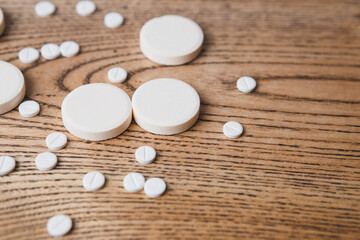 white small and large round pills on a wooden background close-up. Pharmaceutical drugs for the treatment of diseases on a wooden table