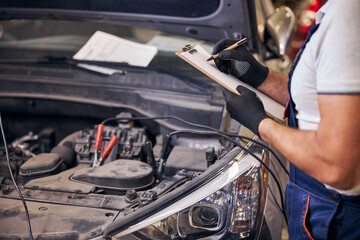 Auto mechanic writing on clipboard in automobile repair shop