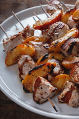 Skewers on wooden skewers of chicken fillet and peaches on a round plate. Rustic food photography