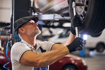 Fototapeta na wymiar Handsome male technician repairing car wheel at service station