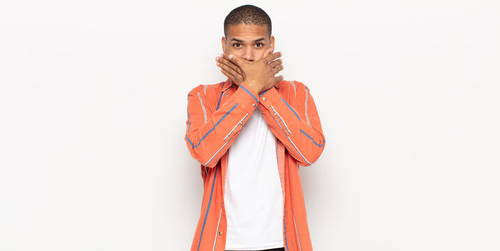 young black man covering mouth with hands with a shocked, surprised expression, keeping a secret or saying oops