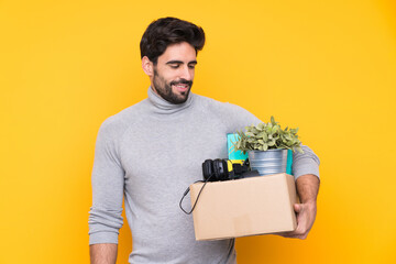 Young handsome man with beard making a move while picking up a box full of things over isolated...