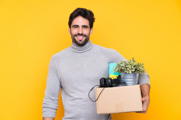 Young handsome man with beard making a move while picking up a box full of things over isolated...