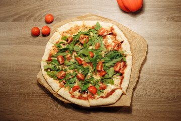 vegan pizza with vegetables on a wooden table in a cafe. Pizza with cherry tomatoes and rucola on food paper on a wooden table with small tomatoes in the foreground and bell pepper in the background