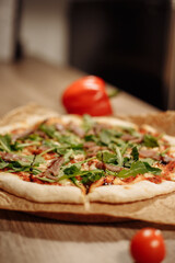 fresh pizza with herbs, tuna and balsamic sauce on food paper on a wooden table in a cozy cafe, bell peppers in the background and cherry tomatoes in the foreground