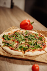 fresh pizza with herbs, tuna and balsamic sauce on food paper on a wooden table in a cozy cafe, bell peppers in the background and cherry tomatoes in the foreground