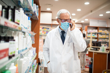 Pharmacist talking on the phone while walking in his pharmacy, coronavirus concept