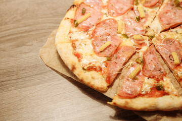 pizza with sausage, mini corn, jalapeno pepper on food paper on a wooden table in warm light
