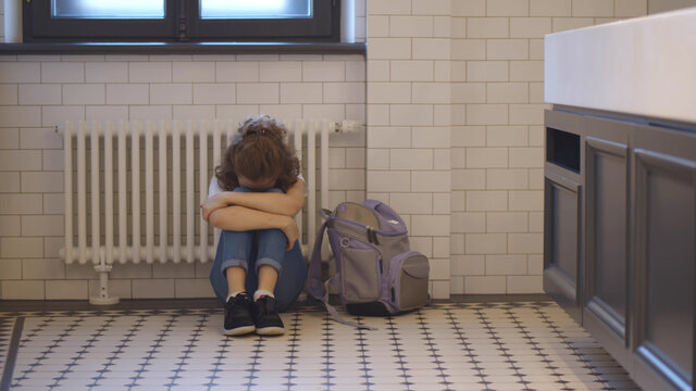 Upset and bullied schoolgirl sitting on floor in restroom and crying