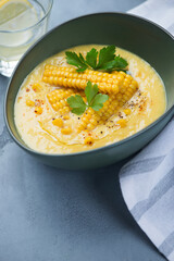 Gazpacho cold soup made of sweet corn and served in a green bowl, vertical shot over grey concrete surface