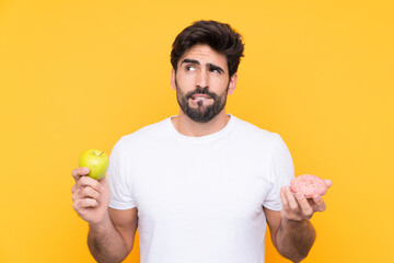 Young handsome man with beard over isolated yellow background having doubts while taking a...