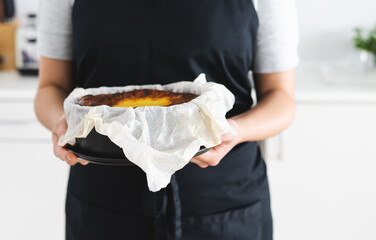 Woman in black apron showing a cheesecake.