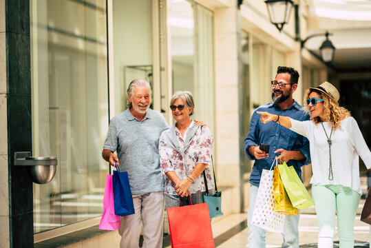 group of four people going shopping together holding shopping bags with presents or gifts for christmas - buying clothes and more in a mall or in some stores