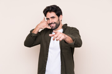 Young handsome man with beard over isolated background making phone gesture and pointing front