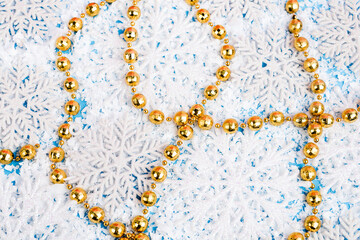 Close up view of golden beads with decorative snowflakes and artificial snow on blue background, new year concept
