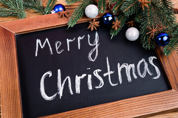Close up view of chalkboard with merry christmas lettering near pine branches, baubles and anise stars on brown wooden background