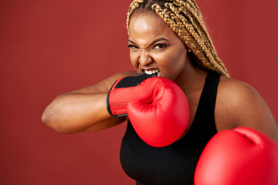 african oversize woman with red boxing mitts isolated on red background, beautiful dark-skinned female boxer training ready to fight