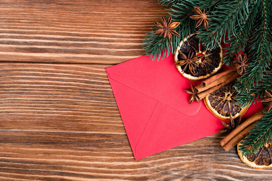 Top view of red envelope near anise stars, cinnamon sticks, dry orange slices and pine branches on brown wooden background