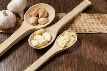 Garlic - Allium sativum; Wooden spoons with garlic; photo on dark wooden background.