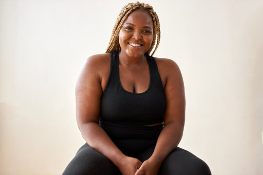 plump, plus size african american young woman in sportswear sit looking at camera, in studio over white background.concept of sport, body positive, equality