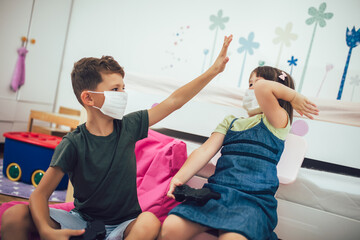 Pretty little girl and boy are playing game console wearing protective mask at home