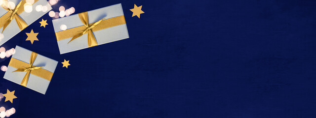 Festive Christmas / Advent background banner panorama - Top view / above view from yellow golden gift boxes with ribbon, stars and bokeh lights, on dark blue paper texture
