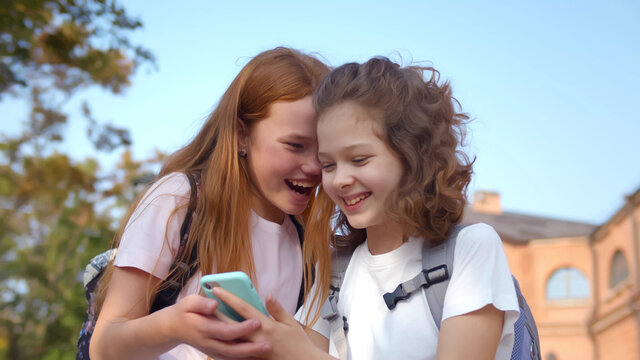 Portrait of cheerful preteen girls using smartphone standing outdoors